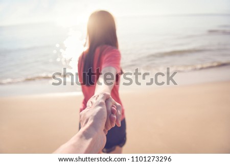 Happy couple on the beach, summer vacations or honeymoon, woman holding hand of husband following her.
