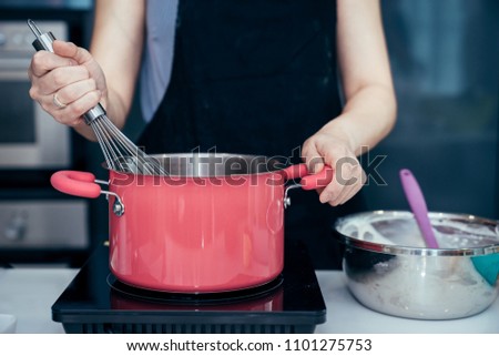 Asian women are chief stirring the ingredients of cake in pink stainless steel pot on an electric stove to making the birthday cake in a family weekend.