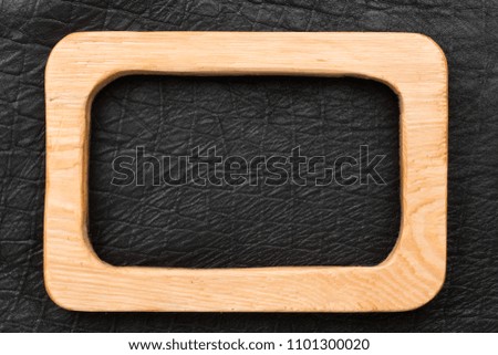 Beautiful wooden frame cut from a light board, lies on a black leather. View from above