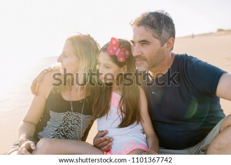 Happy family of father, mother and daughter on the beach at sunset
