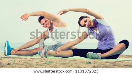 Young russian guy and girl practising yoga poses sitting on beach by sea at daytime