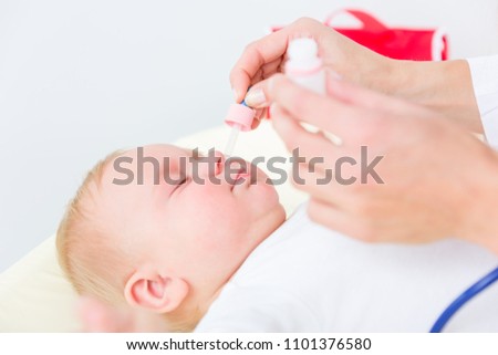 Close-up of the hands of a pediatrician clearing the nose of a baby, by applying saline solution in the nostrils with a nasal aspirator during physical check-up