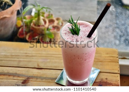 Refreshment delicious and healthy drink for summer, banana and strawberry frappe in glass top with green herb and brown straw place on wooden table blurry plant in brown pot in the garden background  