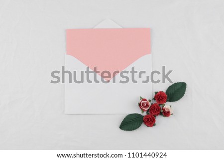 Pink card in white envelop decorate with red rose paper flowers on white fabric 
