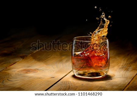 Whiskey splash in glass on a wooden table. Royalty-Free Stock Photo #1101468290