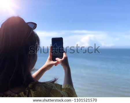 Close up hand of Female holding smartphone and take photo of sea view on summer day. Holiday, vacation and technology concept. Selective focus at hand