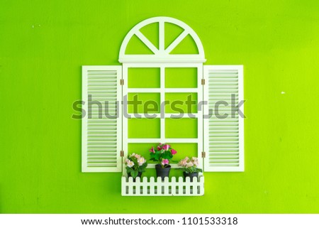 Fake white window decorated with pots of flowers on bright green wall background, concept of creative interior/exterior or home decoration