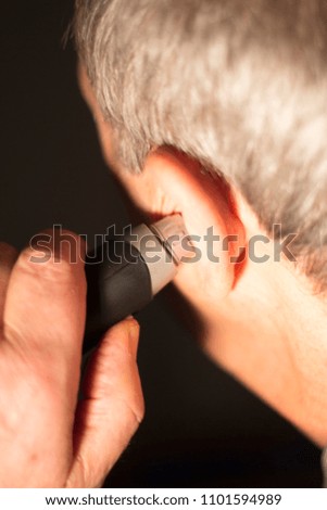 Senior citizen man cutting inner ear hair with electric cutter.