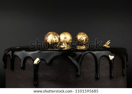 Chocolate cake with black glaze, decorated with balls in gold on a black background. Picture for a menu or a confectionery catalog.