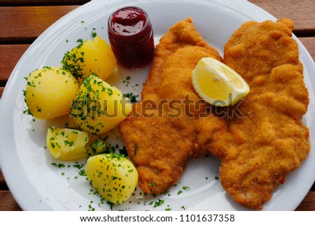 Wiener schnitzel made of pork and served with boiled potatos, cranberry jam and lemon Royalty-Free Stock Photo #1101637358