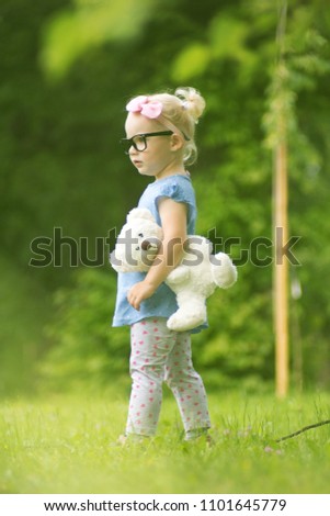 Child little girl with glasses and teddy bear in nature and park, face emotion.