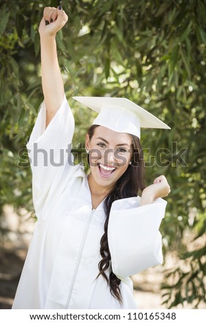 Attractive Smiling Mixed Race Girl Celebrating Graduation Outside In Cap and Gown.