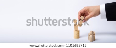 The man's hand of a businessman in a business suit holds a wooden figure of a man in his hand and moves another figure from his post. The concept of firing an employee, the replacement of staff Banner