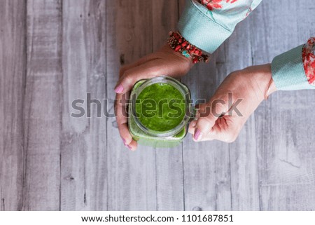 top view of a woman holding a jug with green detox juice. Grey wood table background. Natural and healthy concept