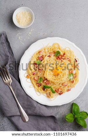 Pasta spaghetti carbonara with bacon, parmesan cheese, egg yolk and basil leaves on gray light background. Traditional Italian dish. Top view.