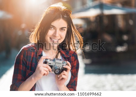 Cute brunette hipster smiling girl holding retro old photo camera, sunset outdoor portrait