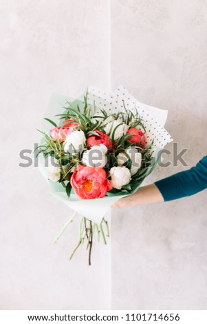 very nice young woman holding a beautiful blossoming flower mono bouquet of fresh peonies and eucalyptus in coral and white colors on the grey wall background