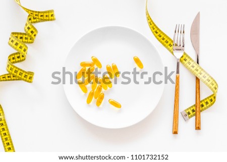Dietary supplement for well-being. Fish oil or omega-3 capsules on plate near measuring tape on white background top view