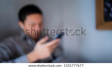 Abstract blurry background of a man wearing gray shirt  resting and relax sitting at side wall listening music  with earphone and smartphone.