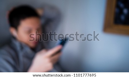 Abstract blurry background of a man wearing gray shirt  resting and relax sitting at side wall listening music  with earphone and smartphone.