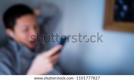 Abstract blurry background of a sleepy man wearing gray shirt relax sitting and yawn at side wall listening music  with earphone and smartphone.
