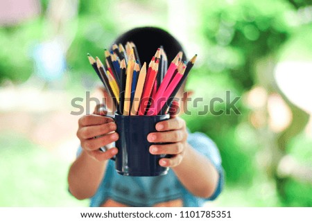 In the hands of the boy holding a black glass, put the crayons back from school. Behind the melting is a beautiful bokeh.