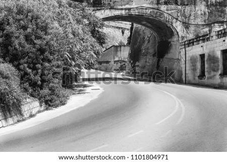 Typical street through the fortress on the island of Malta. Asphalt road under arch in historic part of Valletta. Black and white picture