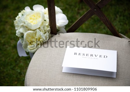 Top down view on a white paper card "Reserved Father of the Bride" sign, on a seat cushion, at a formal outdoor wedding ceremony, with space for text