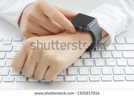 A woman wearing a white shirt with a finger on a smart wrist watch on a wrist in a white room  - stock photo. Intelligent watches, computer monitors, watches, computer wear, computers, keyboards 