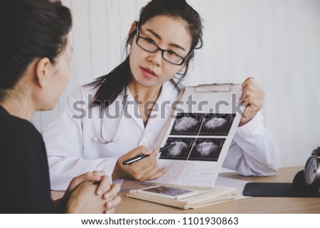 Asian female doctor holding x-ray medical picture explaining the examination and result to patient at a hospital  