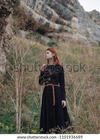 A woman in a black dress walks near dry tree branches