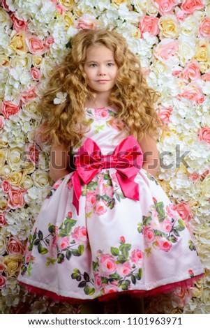 Portrait of a cute little girl in a beautiful summer dress with blonde curly hair. Background of roses. Kid's fashion, style.