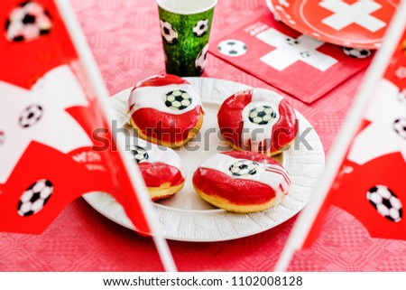 Doughnuts im football theme on red table cloth. Football party at home with snacks and sweets. Football fever worldwide.