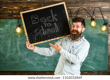 Teacher in eyeglasses holds blackboard with title back to school. Man with beard and mustache on happy face welcomes students, chalkboard on background. High school concept.