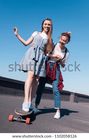low angle view of smiling woman teaching her female friend riding on skateboard 