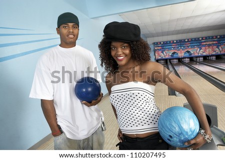 Portrait of two young African American friends at bowling alley holding ball
