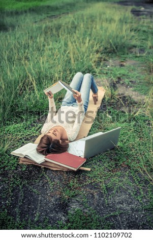 a malay girl is reading a book while laying on grass