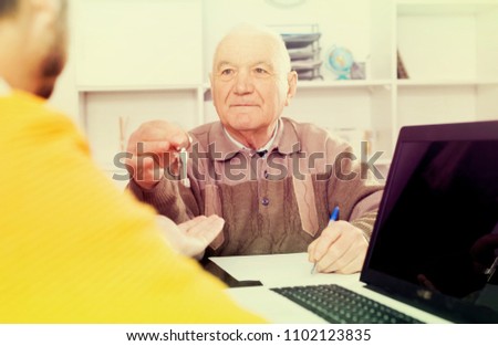 Elderly man and young agent sign lease contract of apartment at office and hand over keys