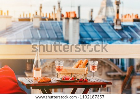Paris luxury lifestyle. Pink wine in two glasses, traditional french bakery products - baguettes, macaron, croissant and strawberries on a balcony with a view on rooftops and Eiffel Tower