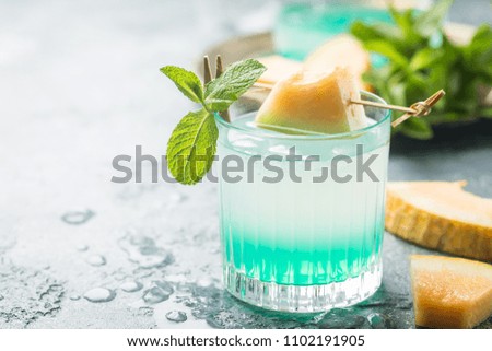 Melon lemonade with ice and mint in a glass on the gray table. Summer refreshing drink.