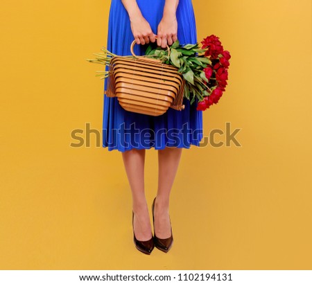 Pretty   European  woman in blue dress holding bouquet of flowers over yellow background. Straw hat. Summer mood. 