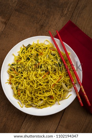 vegetable noodles served in a white plate with sticks on wooden background