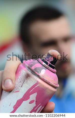 A young graffiti artist in a blue jacket is holding a can of paint in front of him against a background of colored graffiti drawing. Street art and vandalism concept