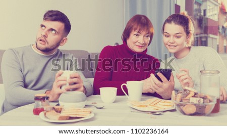 Young man bored at home while his wife and elderly mother absorbedly looking at phones