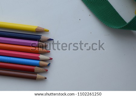 Set of colored pencils and a green webbing from a school backpack on a white table