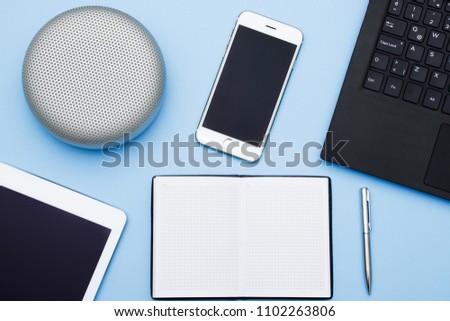 Overhead of office table with laptop, tablet pc, cellphone, speaker and big copy space of notebook, blue flat lays