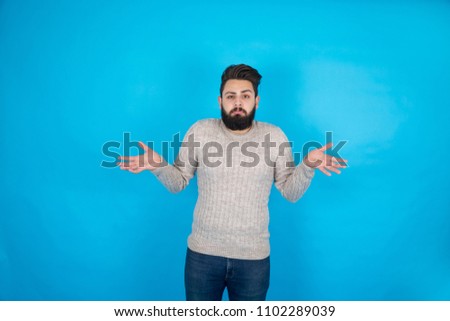 Young man standing raising his two hands wondering on a blue background.