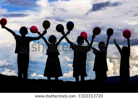 silhouette of children holding air balloons playing in park at summer