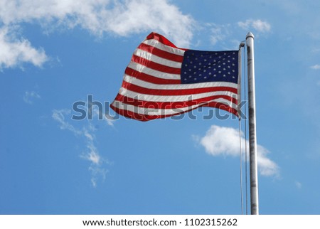 American flag on pole flying to the left in front of blue sky and white clouds