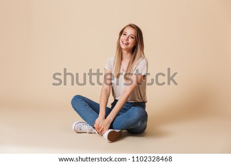 Image of beautiful woman wearing casual clothing smiing while sitting on floor with legs crossed isolated over beige background Royalty-Free Stock Photo #1102328468